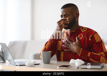 Sintomi del coronavirus. Black Freelancer Guy in costume etnico sentirsi male a casa Foto Stock