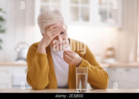 Donna anziana che soffre di mal di testa, prendendo la pillola Foto Stock