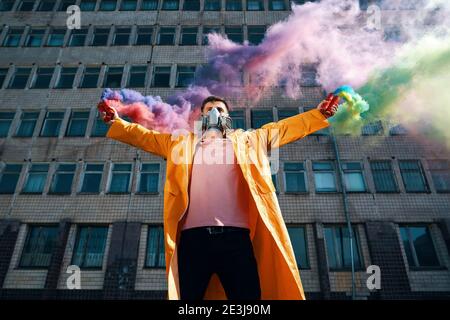 Il giovane uomo in maschera respiratore regge bombe di fumo in mani alzate. Protesta, libertà, concetto di rivoluzione Foto Stock