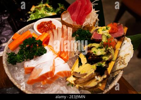 Assortimento di sashimi serviti su ghiaccio in ciotola di ceramica giapponese delicatezza costituita da pesce fresco crudo o carne affettata pezzi sottili e mangiati con soia Foto Stock