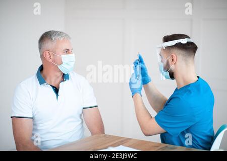 Immunizzazione per gli anziani. Uomo posteriore in visita al medico, preparandosi per l'iniezione del vaccino del coronavirus in clinica Foto Stock