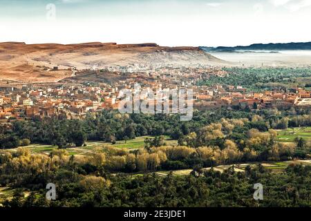 Vista panoramica aerea di oasi con fiume e Tinghir berber villaggio nel deserto del sahara contro canyon, Marocco Foto Stock