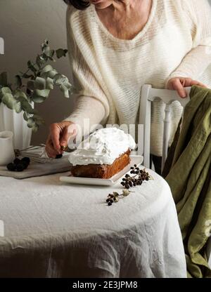 Pound torta, donna fatta decorare con glassa bianca, moderna vita morta sul tavolo bianco e sedia bianca. Eucalipto Foto Stock