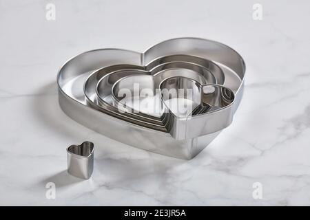 Set di tagliacinette a forma di cuore in acciaio inox su un bianco superficie in marmo Foto Stock