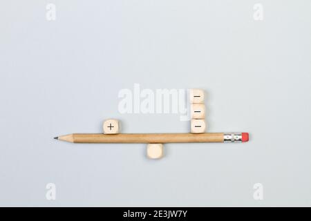 Meno e più segni cubetti di legno con una matita in modo equilibrato su uno sfondo grigio Foto Stock