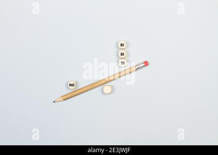 Sì e no parola cubetti di legno con una matita in modo equilibrato su uno sfondo grigio (sì-no) Foto Stock