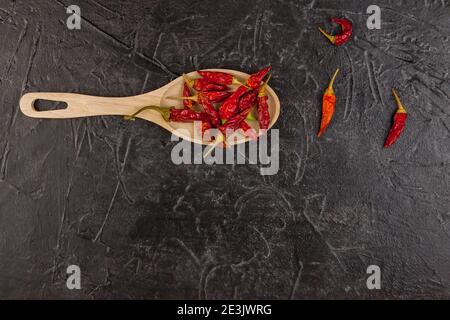 Un cucchiaio di legno con peperoncino rosso essiccato giace su fondo nero. Spazio per il testo Foto Stock