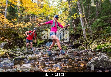 Uomo e donna Trail corridori rock-hopping in un fiume con caduta fogliame Foto Stock