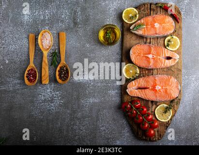 tre trote crude di pesce bistecca, salmone e spezie su tavola di legno, sfondo scuro Foto Stock