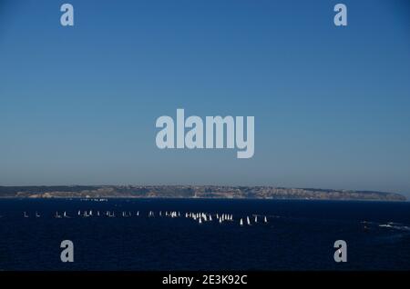 molte barche a vela bianche con costa rocciosa nel mare blu Foto Stock