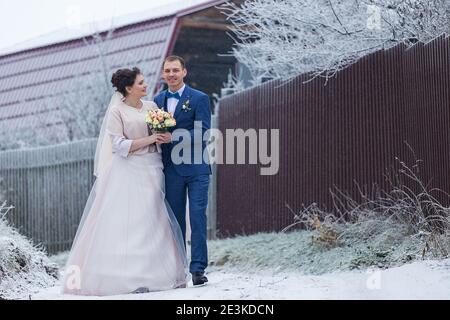 sposi in una passeggiata di nozze in inverno stand insieme e posa per un fotografo vicino a un albero coperto di neve in una bella foresta, la famiglia scatta una foto Foto Stock