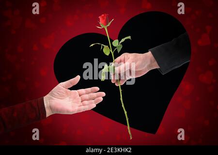 Mano di un uomo sta dando una rosa attraverso un buco nero a forma di cuore in un biglietto d'auguri rosso alla mano di una donna il giorno di San Valentino, concetto d'amore Foto Stock