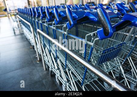 Maniglie blu di carrelli per la spesa in fila in attesa di clienti di fronte a un negozio al dettaglio durante la chiusura a causa di covid-19 pandemia, spazio di copia, selecte Foto Stock