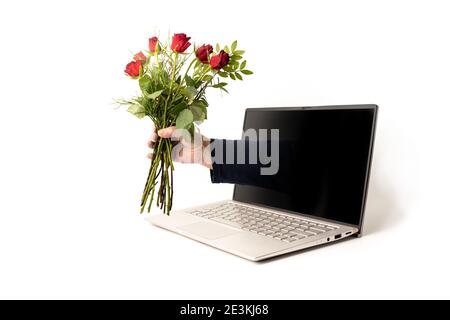 Mano di un uomo con un bouquet di rose rosse uscenti dallo schermo di un laptop, amore digitale nella giornata di San Valentino con distanza sociale durante la pandemia covid-19, Foto Stock
