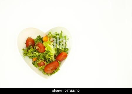 Lattuga mescolata con pomodori ciliegini rossi in una ciotola a forma di cuore cibo vegano biologico Foto Stock