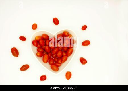 Cuore rosso formato da pomodori ciliegini rossi contenuti in A. piatto gourmet a forma di cuore Foto Stock