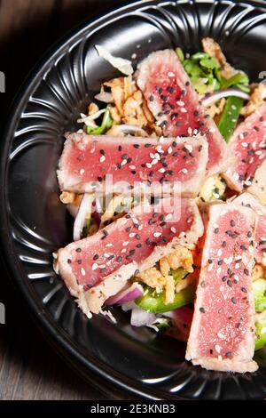 Insalata di tonno scottato con lattuga, peperone verde a fette e cipolla rossa su un tavolo di legno Foto Stock