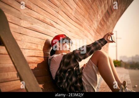 adolescente asiatico skateboarder ragazzo prendendo un selfie utilizzando il cellulare Foto Stock