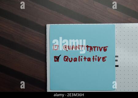 Scrittura quantitativa e qualitativa su note appiccicose e supportata da servizi aggiuntivi scrivono su note appiccicose isolate su tavola di legno. Foto Stock