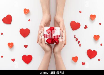 Le mani dell'uomo e della donna tengono la scatola del regalo su sfondo bianco. Amore e concetto di San Valentino. Un uomo dà un dono ad una donna. Vista dall'alto, disposizione piatta. Foto Stock