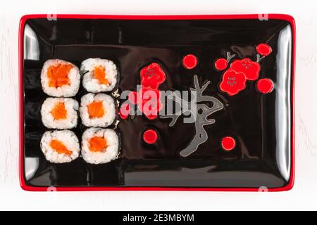 involtini appetitosi freschi con salmone in nori alghe in piatti nero-rosso su un piatto bianco. vista dall'alto Foto Stock