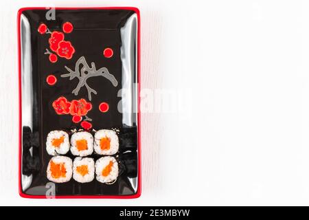involtini appetitosi freschi con salmone in nori alghe in piatti nero-rosso su un piatto bianco. vista dall'alto Foto Stock