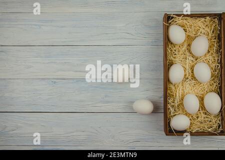 Sette uova di pollo giacciono in una scatola di legno sulla paglia e due l'una accanto all'altra su uno sfondo di legno blu. La vista dall'alto e lo spazio vuoto per il testo Foto Stock