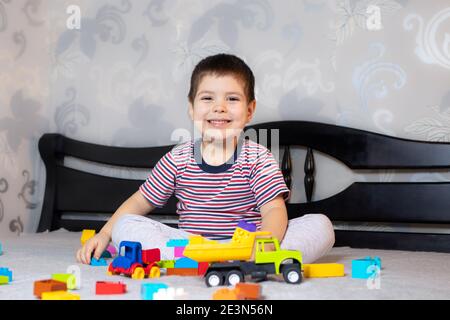 Un bambino in una t-shirt a righe luminose gioca con blocchi multicolore di designer di plastica. Sviluppo di giochi per bambini. Foto Stock