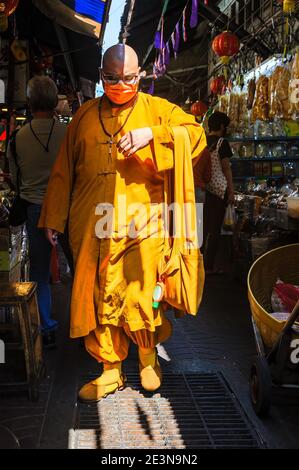 Chinatown, Bangkok, Thailandia - 14 novembre 2020: Un monaco cinese, con un facemask protettivo, cammina con cautela attraverso uno stretto vicolo mercato posto. Foto Stock