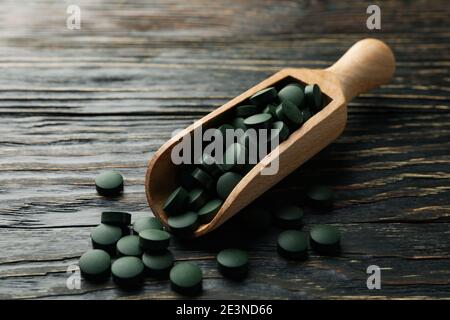 Paletta di legno con pillole di spirulina su sfondo di legno, primo piano Foto Stock