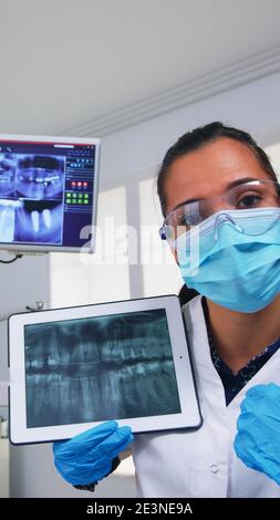 Dentista che mostra sui denti della compressa raggi X esaminandola con il paziente. Medico e infermiere che lavorano insieme in una moderna clinica stomatologica, spiegando alla donna anziana radiografia del dente utilizzando notebook display Foto Stock