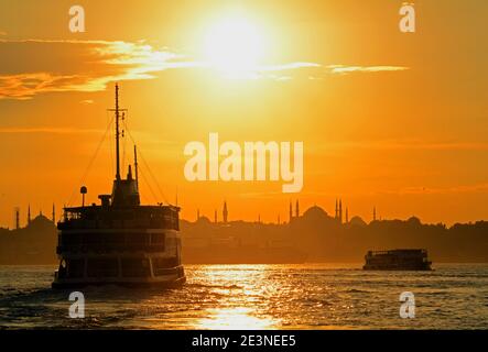 Tramonto a Istanbul, meravigliosa luce dorata mentre i traghetti portano i passeggeri verso la parte vecchia della città con la Moschea Blu in lontananza. Foto Stock