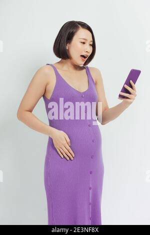 Donna incinta stupita che guarda contenuti multimediali in uno smartphone Foto Stock