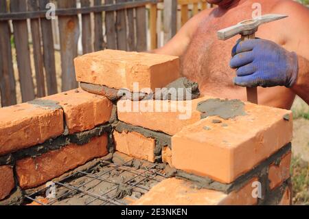 Una persona di muratore sta mettendo una parete della casa di mattone con la rete rinforzata, il filo usando un cazzuola ed un martello di muratura. Foto Stock