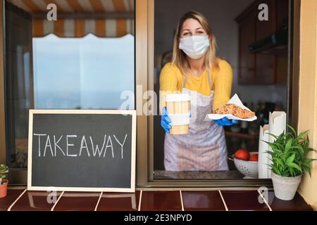 Giovane donna che prepara colazione da asporto e caffè all'interno del panificio Mentre si indossa una maschera di sicurezza - concentrarsi sul cibo Foto Stock