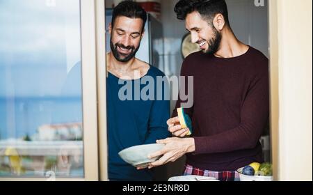 Vista finestra di piatti di lavaggio coppia gay all'interno della cucina casalinga - mettere a fuoco sui volti Foto Stock