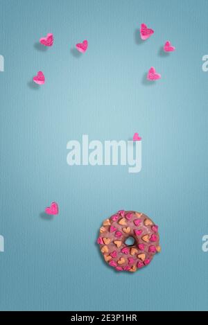 Ciambella rosa smaltata con cuori di marshmallow. Pochi cuori stanno volando intorno. Sfondo carta blu testurizzato. Modello per il biglietto d'auguri di San Valentino con Foto Stock