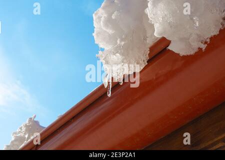 Le ghiacciate pendono dal tetto contro il cielo blu in una soleggiata giornata di primavera. Foto Stock