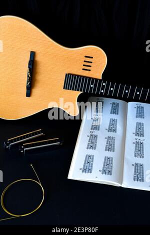 Un piatto musicale si stese su sfondo nero, con una chitarra acustica in legno, armoniche e un libro di tablature. Foto Stock
