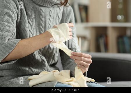 Primo piano delle mani della donna ferita che rimuove il bendaggio dal braccio a casa Foto Stock