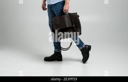 Borsa marrone da uomo in pelle a spalla per documenti e portatili da uomo in una camicia blu e jeans con sfondo bianco. Borsa a mano, pelle da uomo Foto Stock