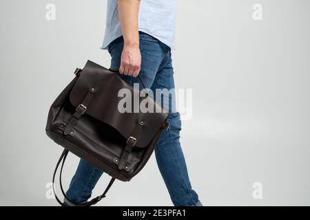 Borsa marrone da uomo in pelle a spalla per documenti e portatili da uomo in una camicia blu e jeans con sfondo bianco. Borsa a mano, pelle da uomo Foto Stock