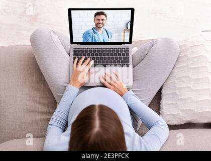 Medicina remota. Vista dall'alto di una donna incinta che riceve assistenza medica su Internet, consultando il medico sul computer portatile da casa Foto Stock