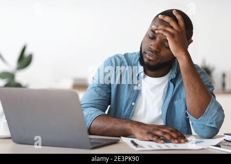 Stressato nero imprenditore maschio che ha problemi al lavoro, seduta sconvolto in ufficio Foto Stock