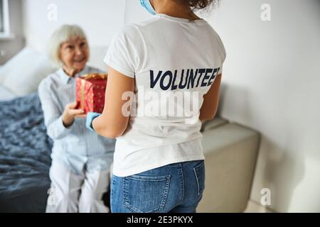 Persona in una camicia volontaria che consegna una scatola presente Foto Stock