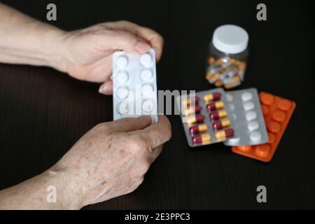 Donna anziana con pillole in mani stropicciate. Farmaci diversi in compresse e capsule, prendendo sedativi, antibiotici o vitamine Foto Stock