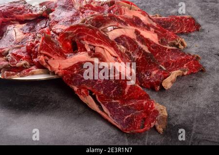 Fette di carne cruda tagliate sottili su un piatto bianco, fondo grigio Foto Stock