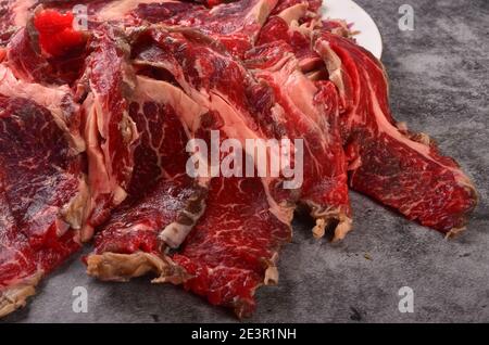 Fette di carne cruda tagliate sottili su un piatto bianco, fondo grigio Foto Stock