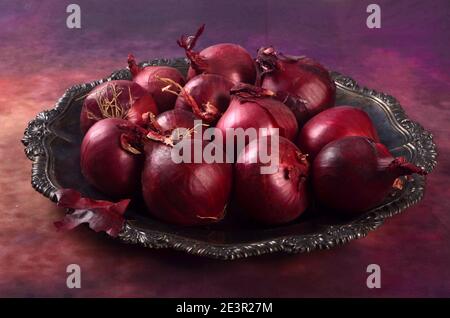 Diverse cipolle rosse su un piatto di metallo, sfondo viola. Ancora vita con cipolle rosse Foto Stock