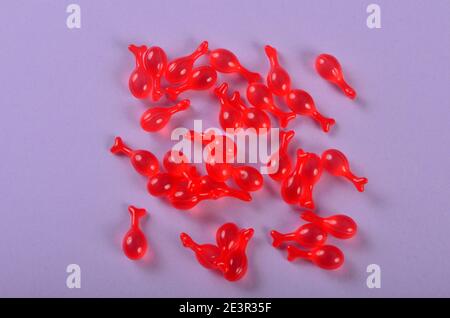 Capsule farmaceutiche di gelatina rossa morbida su sfondo viola. Capsula polipeptidica Caviar Essence liquido diluisce le linee sottili che brigano Foto Stock